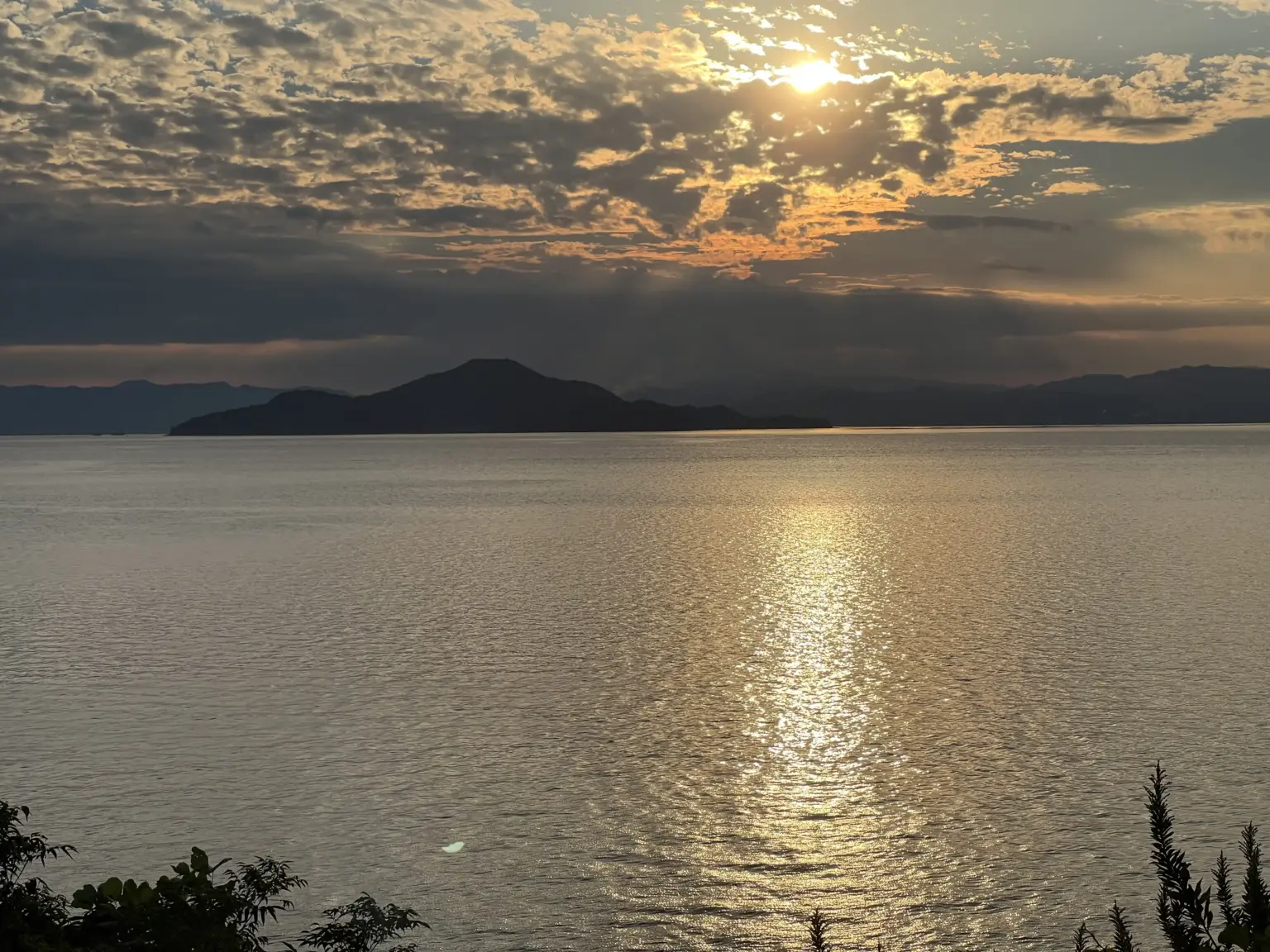 江田島の海に沈む夕日。雲の切れ間から太陽が差し、水平線には島の影が見えます